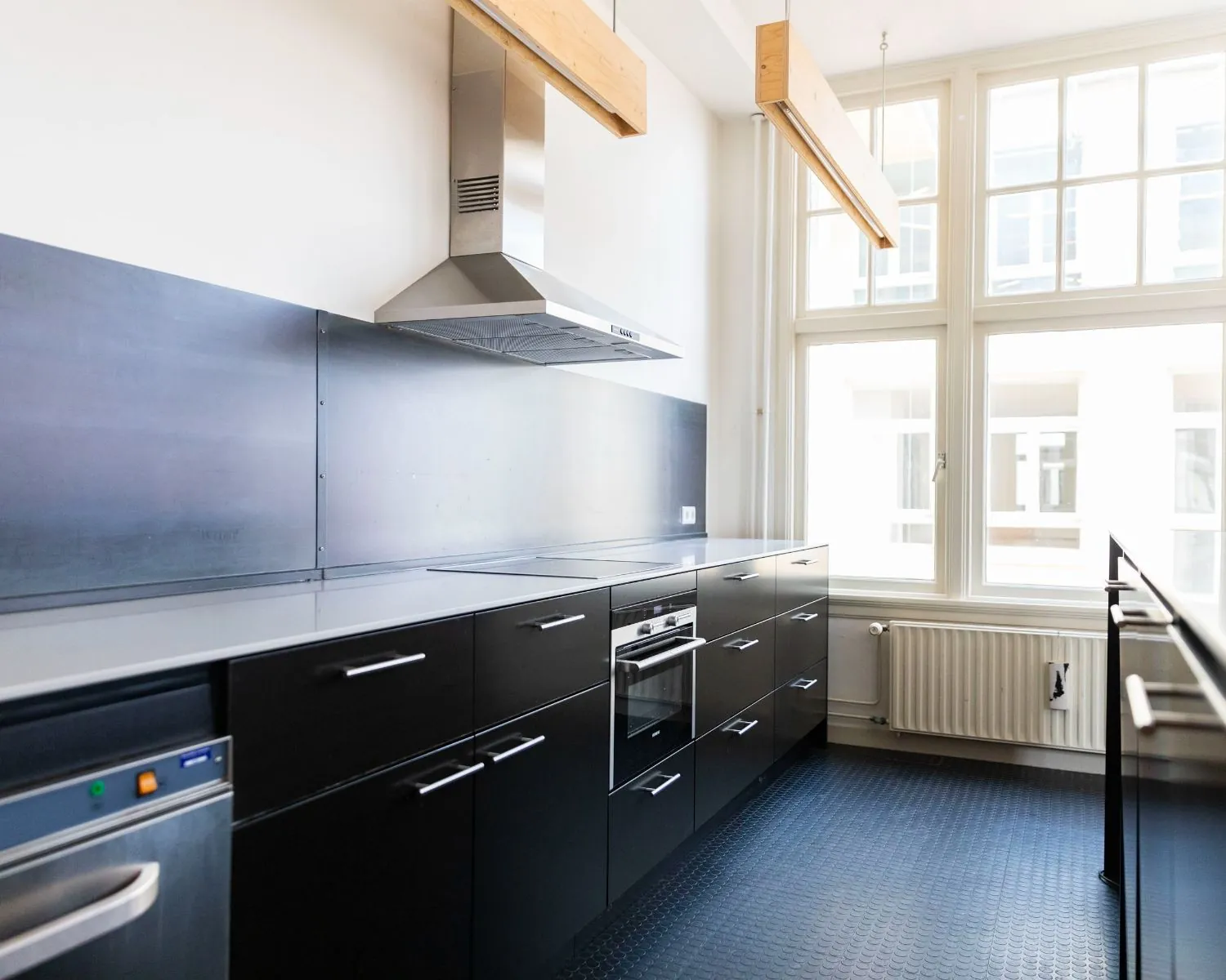 Moderne keuken in een kantoorruimte aan de Prins Hendrikkade 21-9 in Amsterdam met zwarte kasten, RVS-afzuigkap en grote ramen.