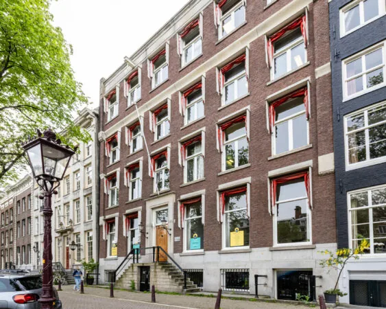 Voorgevel van het kantoorpand aan de Singel 126-130 in Amsterdam met klassieke rode zonweringen en bordjes in de ramen.