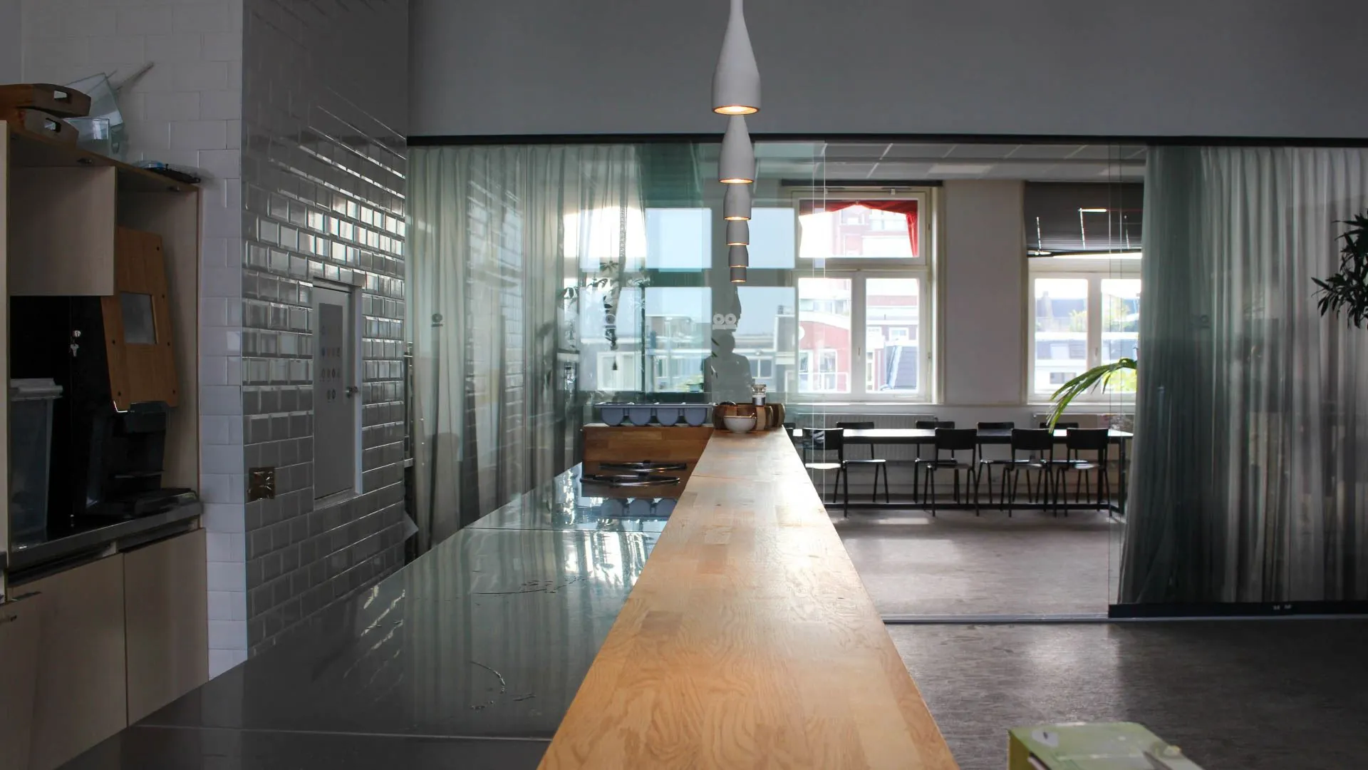 Moderne kantoorruimte aan het Singel in Amsterdam met een lange houten bar, glazen wanden en uitzicht op een vergaderruimte met grote ramen.