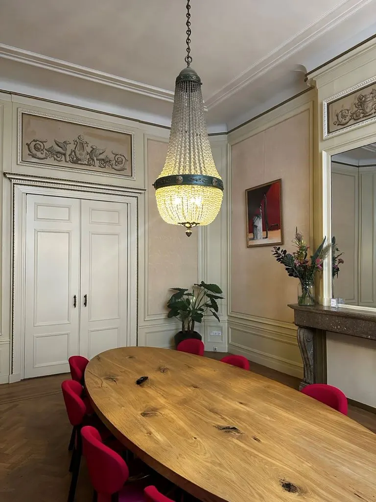 Vergaderkamer met ovale houten tafel, rode stoelen en een klassieke kroonluchter in een stijlvol kantoor aan het Singel 126-130 in Amsterdam.