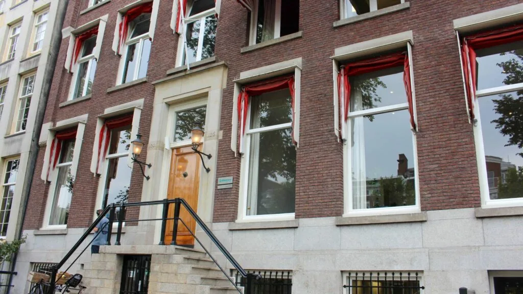 Voorgevel van het kantoorpand aan het Singel 126-130 in Amsterdam met rode markiezen en een stenen trap naar de entree.