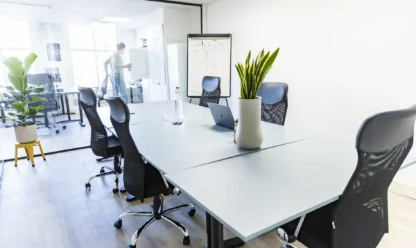 Moderne vergaderruimte met zes bureaustoelen, glazen wand en een persoon werkend bij een whiteboard in kantoorruimte Amsterdam Singel 126-130.