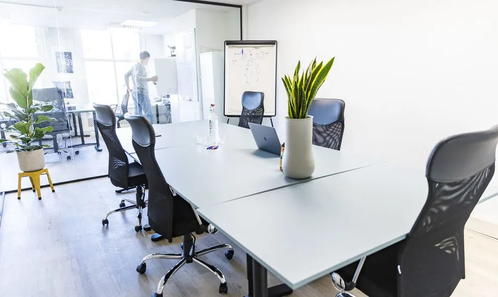 Moderne vergaderruimte met zes bureaustoelen, glazen wand en een persoon werkend bij een whiteboard in kantoorruimte Amsterdam Singel 126-130.