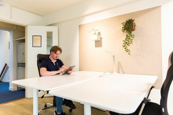Moderne kantoorruimte aan het Singel in Amsterdam met een man die op een tablet werkt aan een wit bureau.