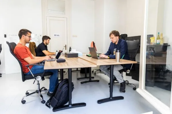 Drie personen werken op laptops in een moderne kantoorruimte aan de Singel 126-130 in Amsterdam.