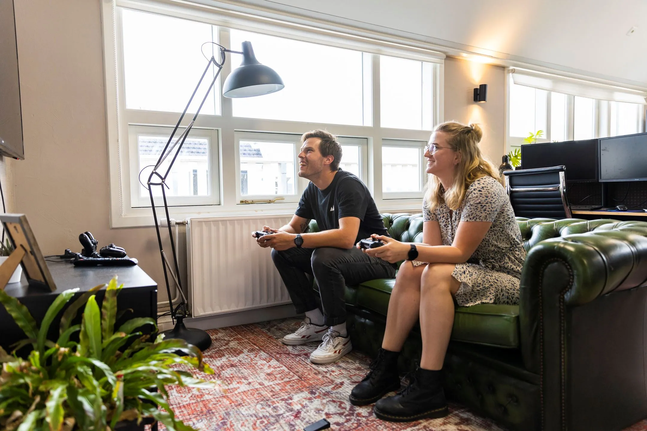 Twee mensen zitten op een groene bank in een kantoorruimte aan het Singel 126-130 in Amsterdam en spelen een videogame.