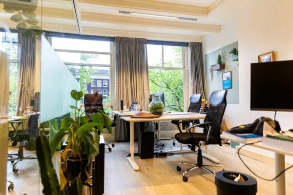 Moderne kantoorruimte aan het Singel in Amsterdam met werkplekken, planten en grote ramen met uitzicht op grachtenpanden.