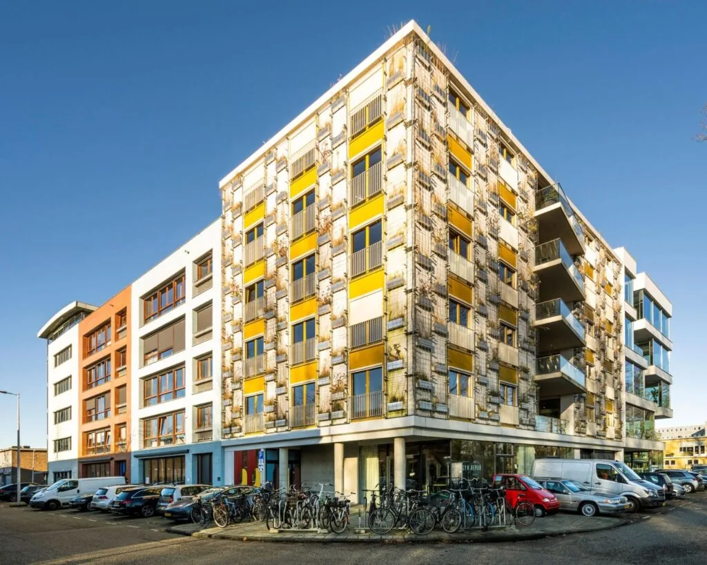 Modern kantoorgebouw aan de Vliegtuigstraat 6-1 in Amsterdam met een opvallende gevel en geparkeerde fietsen en auto's ervoor.