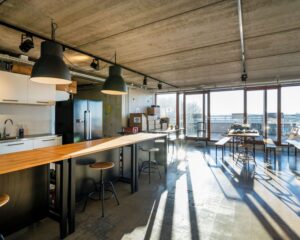 Moderne kantoorruimte aan de Vliegtuigstraat in Amsterdam met open keuken, hoge tafels, industriële verlichting en grote ramen met veel daglicht.
