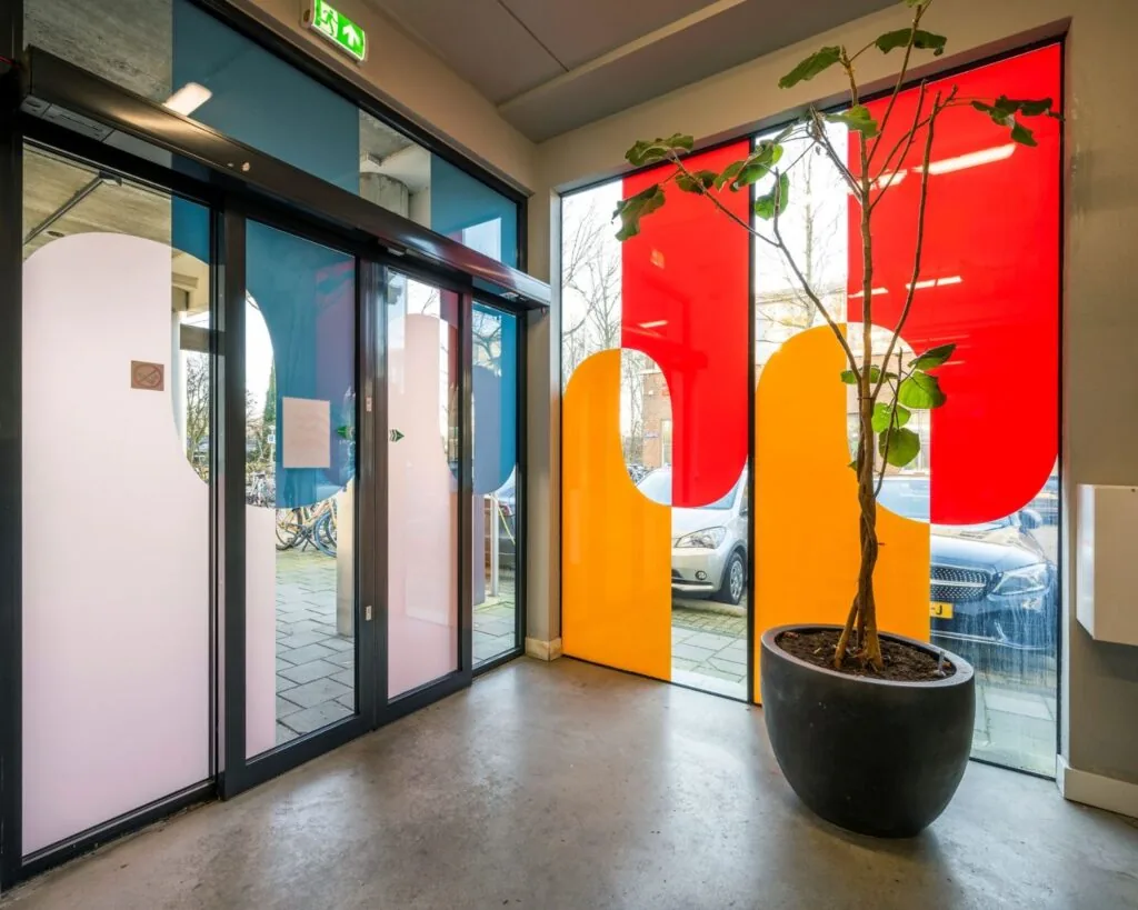 Ingang van een moderne kantoorruimte aan de Vliegtuigstraat in Amsterdam met gekleurde raamfolie en een grote plantenbak.