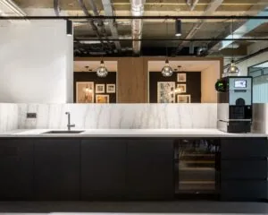 Moderne pantry met marmeren achterwand, zwarte keukenkastjes en een koffiemachine in een kantoorruimte aan de Weerdestein 97 in Amsterdam.