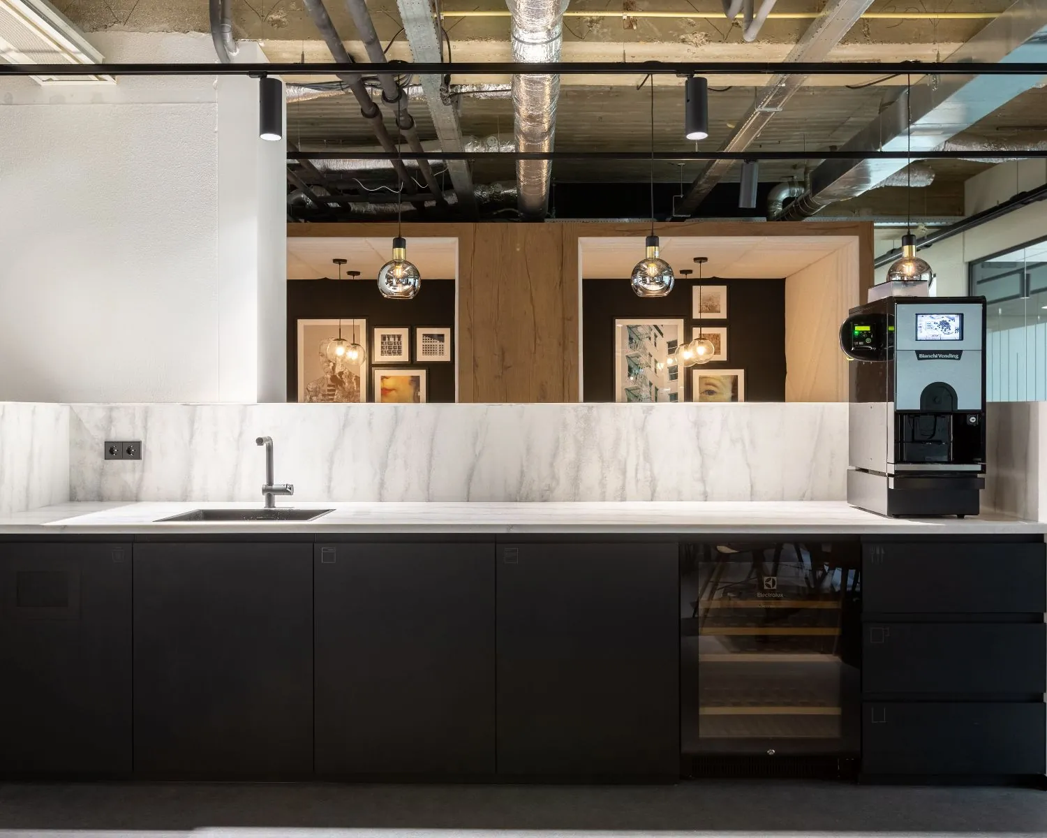 Moderne pantry met marmeren achterwand, zwarte keukenkastjes en een koffiemachine in een kantoorruimte aan de Weerdestein 97 in Amsterdam.