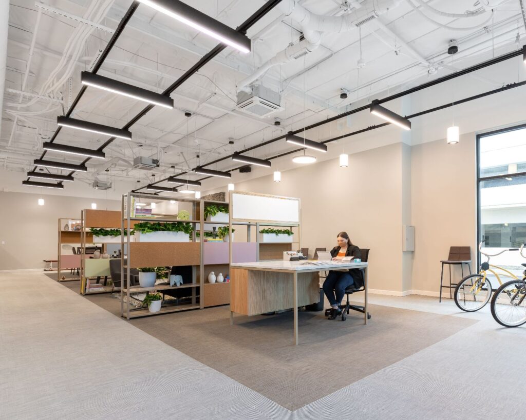 Moderne kantoorruimte te huur aan de Haarlemmerweg 331 in Amsterdam met open werkplekken, planten en een vrouw aan het werk.