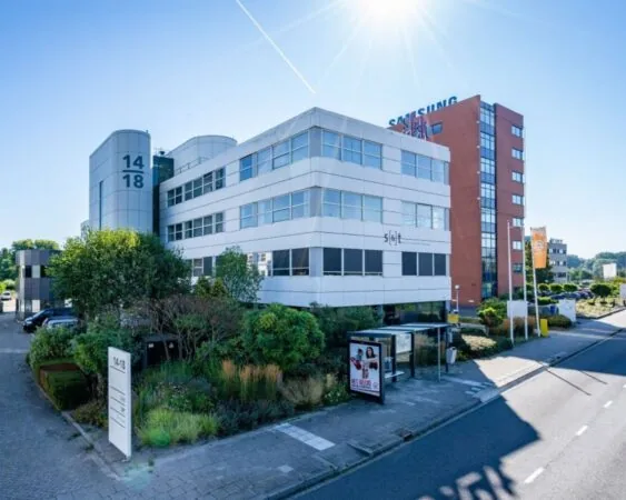 Modern kantoorpand aan de Olof Palmeweg 14-18 in Delft met beplanting en bushalte op de voorgrond.