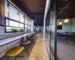 Moderne kantoorruimte in Delft met grote ramen, houten vloer, zitplekken langs het raam en een vergaderruimte met glazen wand.