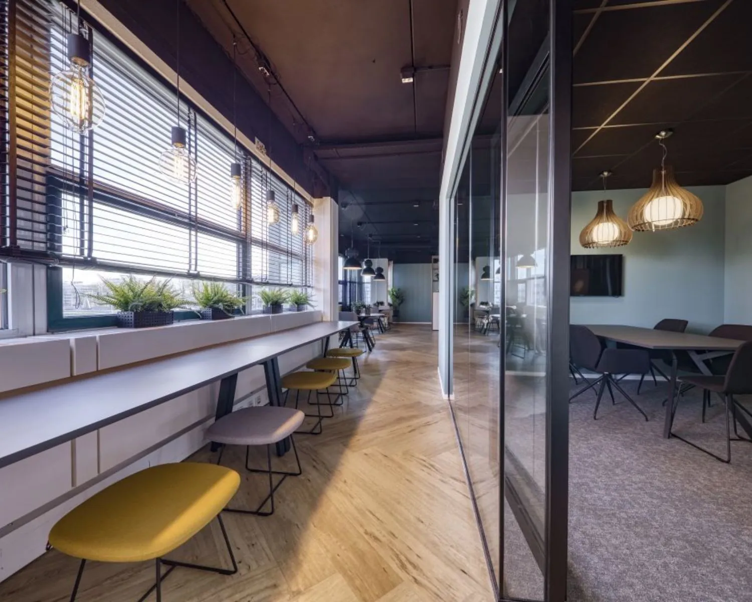 Moderne kantoorruimte in Delft met grote ramen, houten vloer, zitplekken langs het raam en een vergaderruimte met glazen wand.