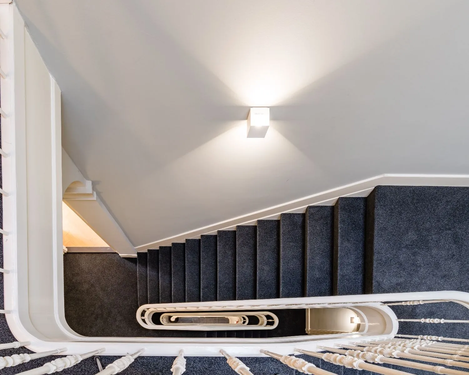 Doorkijk vanuit een trapgat op een stijlvol trappenhuis met donker tapijt in een kantoorruimte aan de Alexanderstraat in Den Haag.