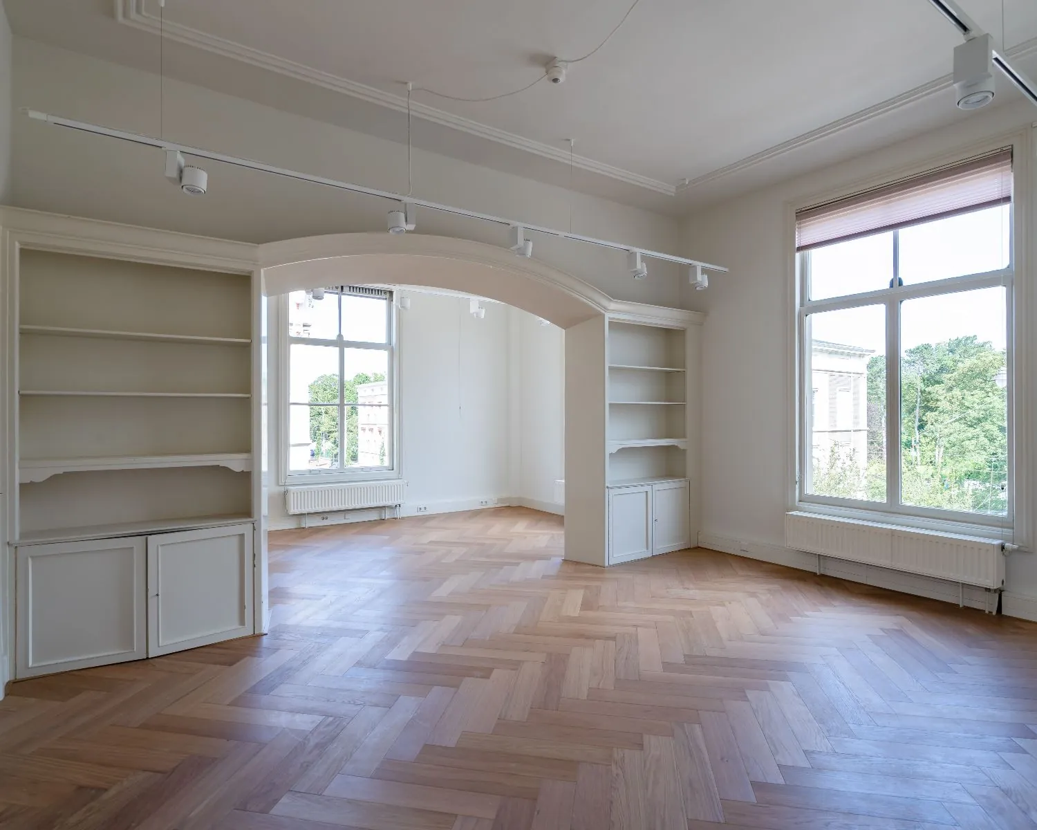 Lichte kantoorruimte aan de Alexanderstraat in Den Haag met visgraatvloer, grote ramen en ingebouwde kasten.