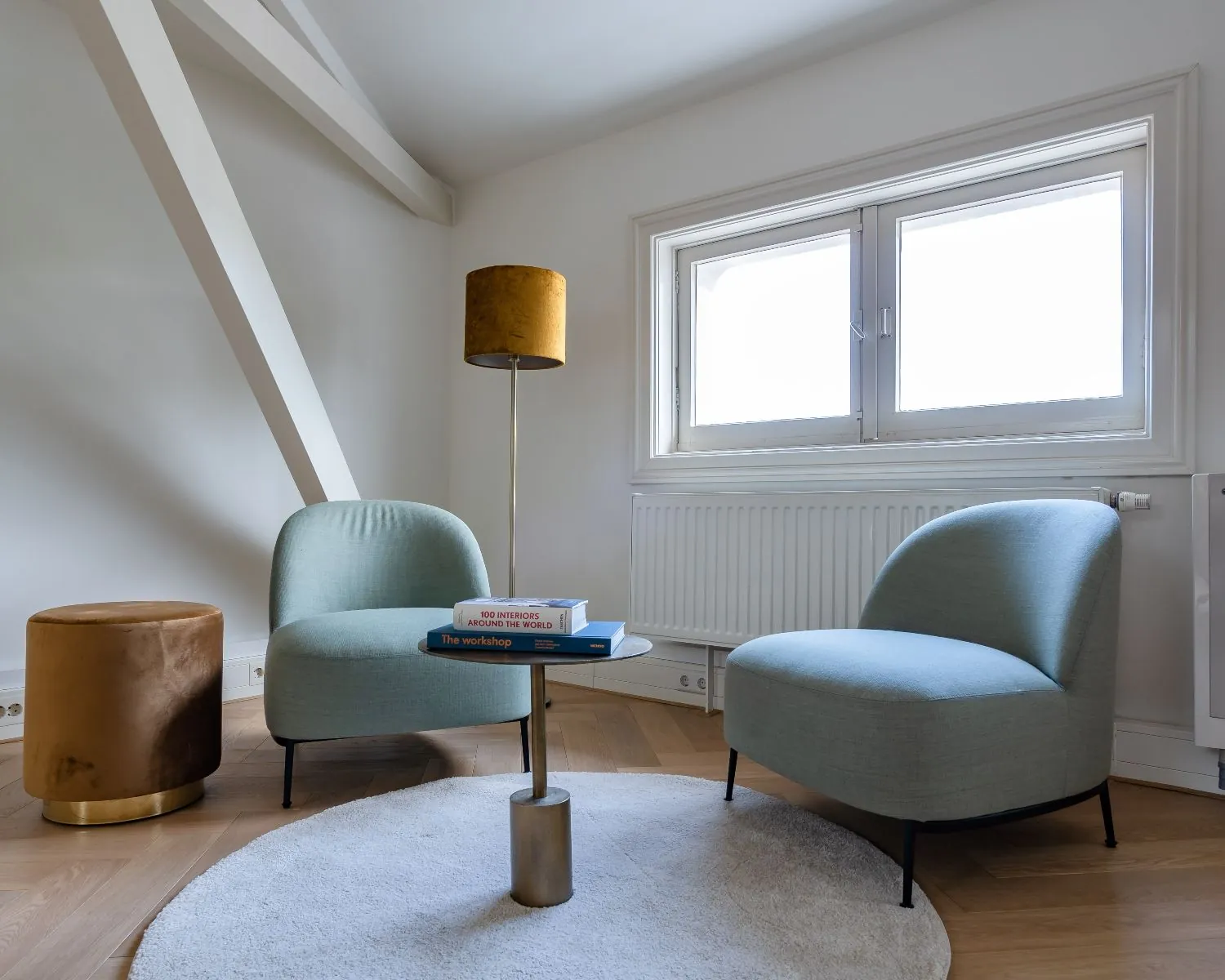 Moderne kantoorruimte in Den Haag met twee lichtblauwe fauteuils, een ronde vloerlamp en bijzettafel in een sfeervolle zithoek.