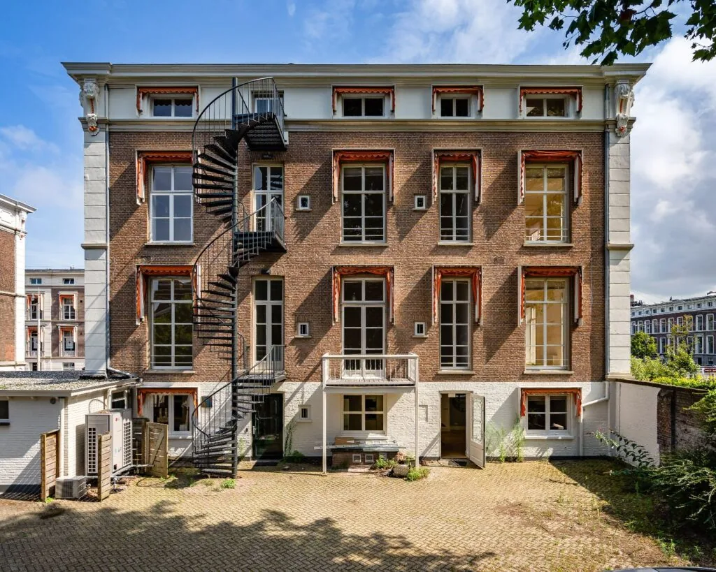 Achterzijde van een klassiek kantoorpand aan de Alexanderstraat 4-6 in Den Haag met een wenteltrap en meerdere hoge ramen.