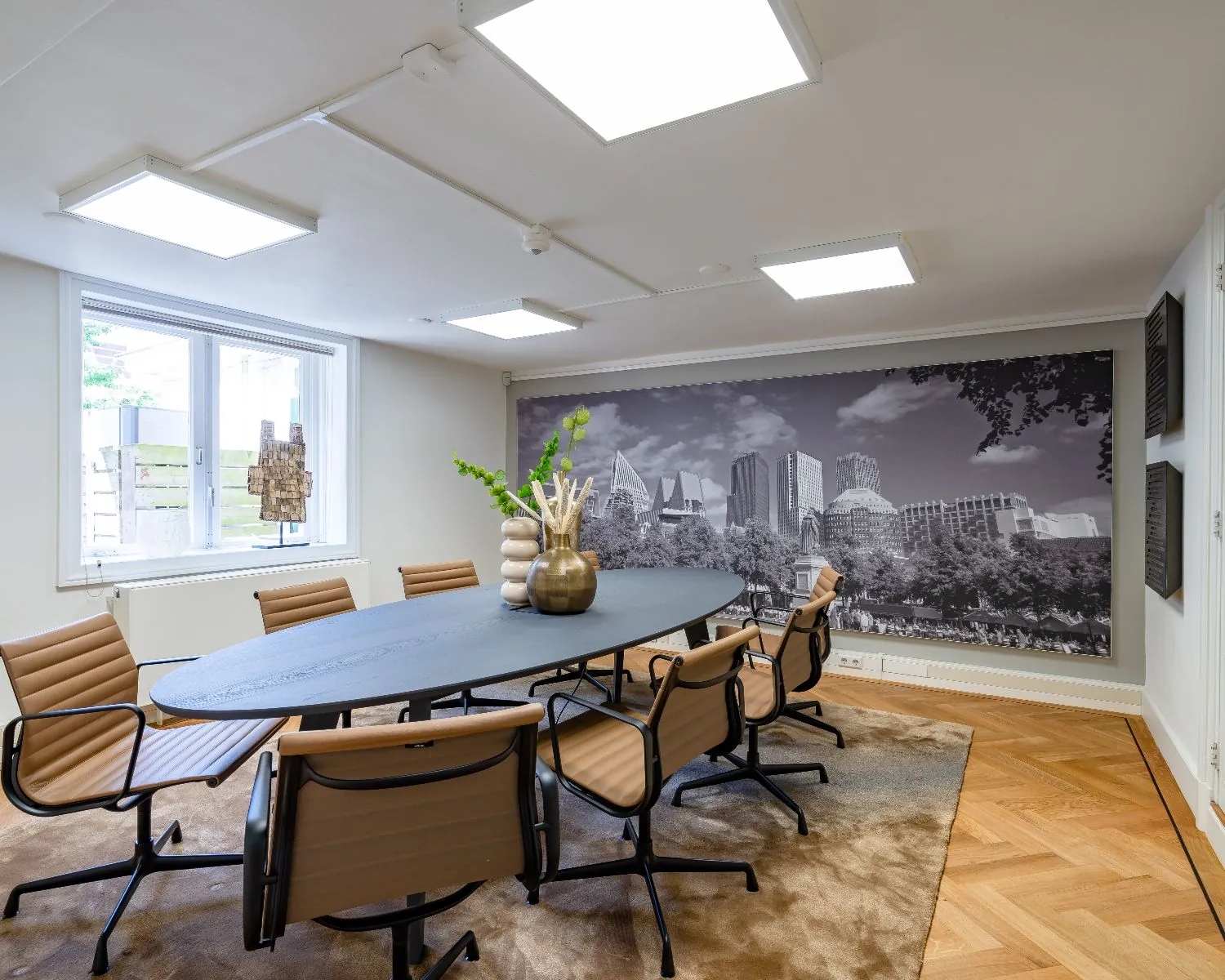 Moderne vergaderruimte in een kantoor aan de Alexanderstraat in Den Haag met ovale tafel, leren stoelen en muurdecoratie van de Haagse skyline.