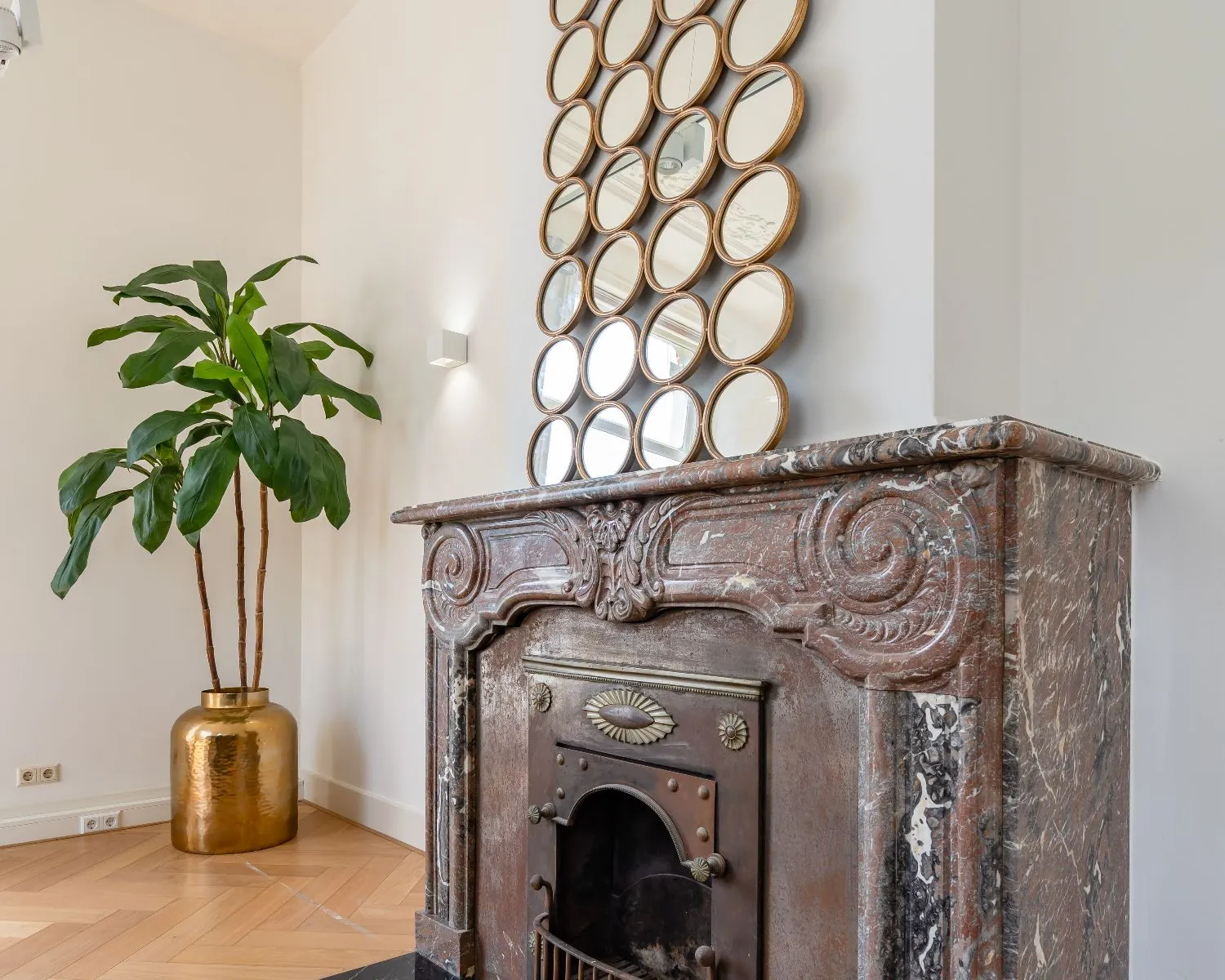 Decoratieve open haard met marmeren omlijsting en ronde spiegels in kantoorruimte aan de Alexanderstraat in Den Haag.