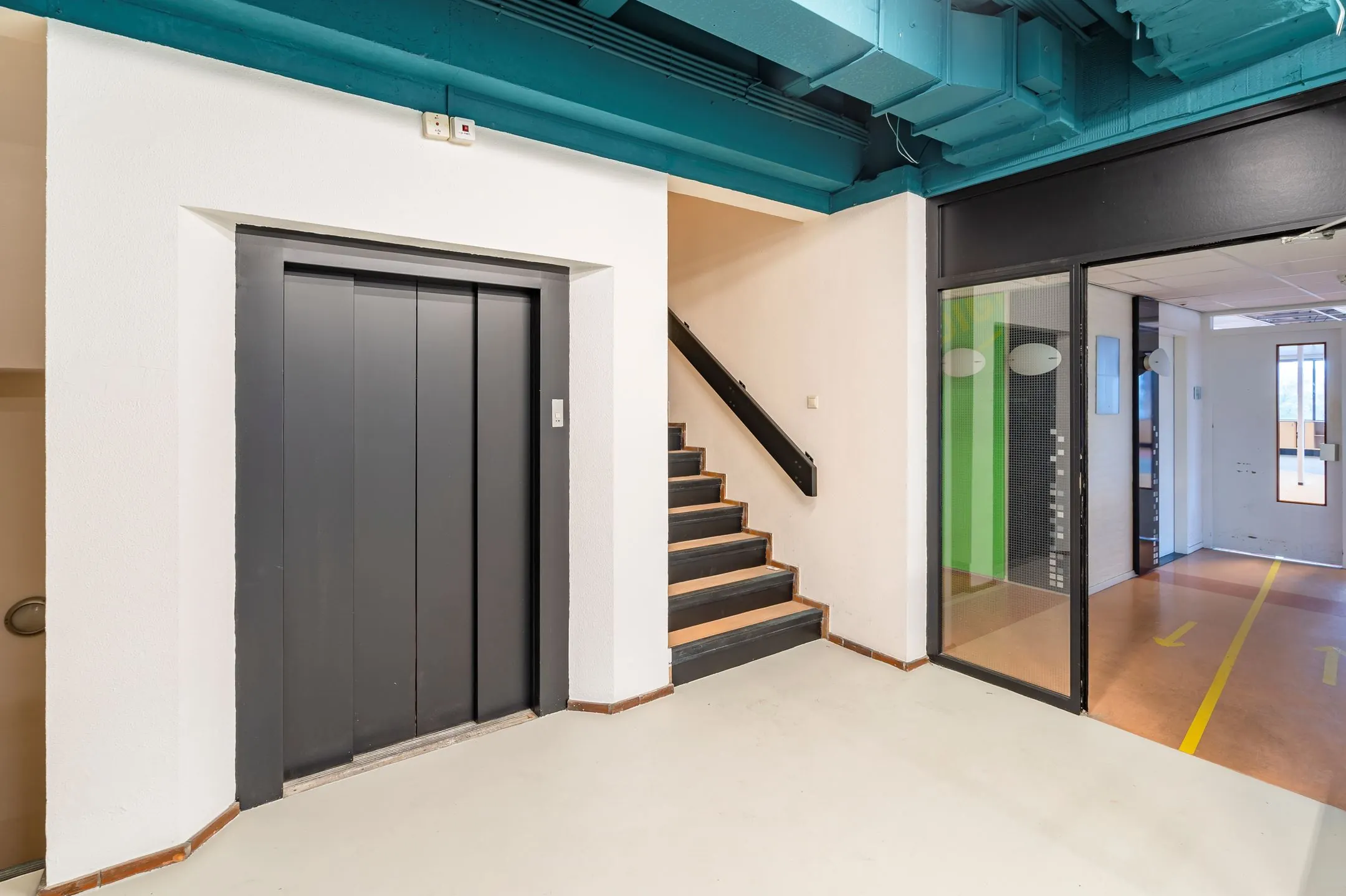 Entreehal met een lift, trap en glazen deur in een kantoorruimte aan de Staverenstraat 15-17 in Deventer.