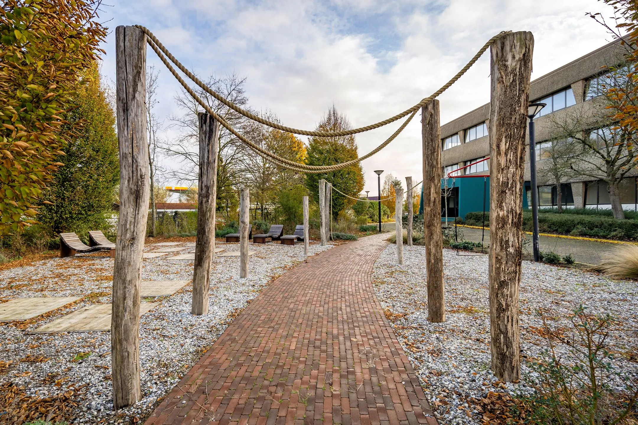 Buitenruimte met wandelpad, houten palen met touwconstructie en ligstoelen bij kantoor aan de Staverenstraat 15-17 in Deventer.
