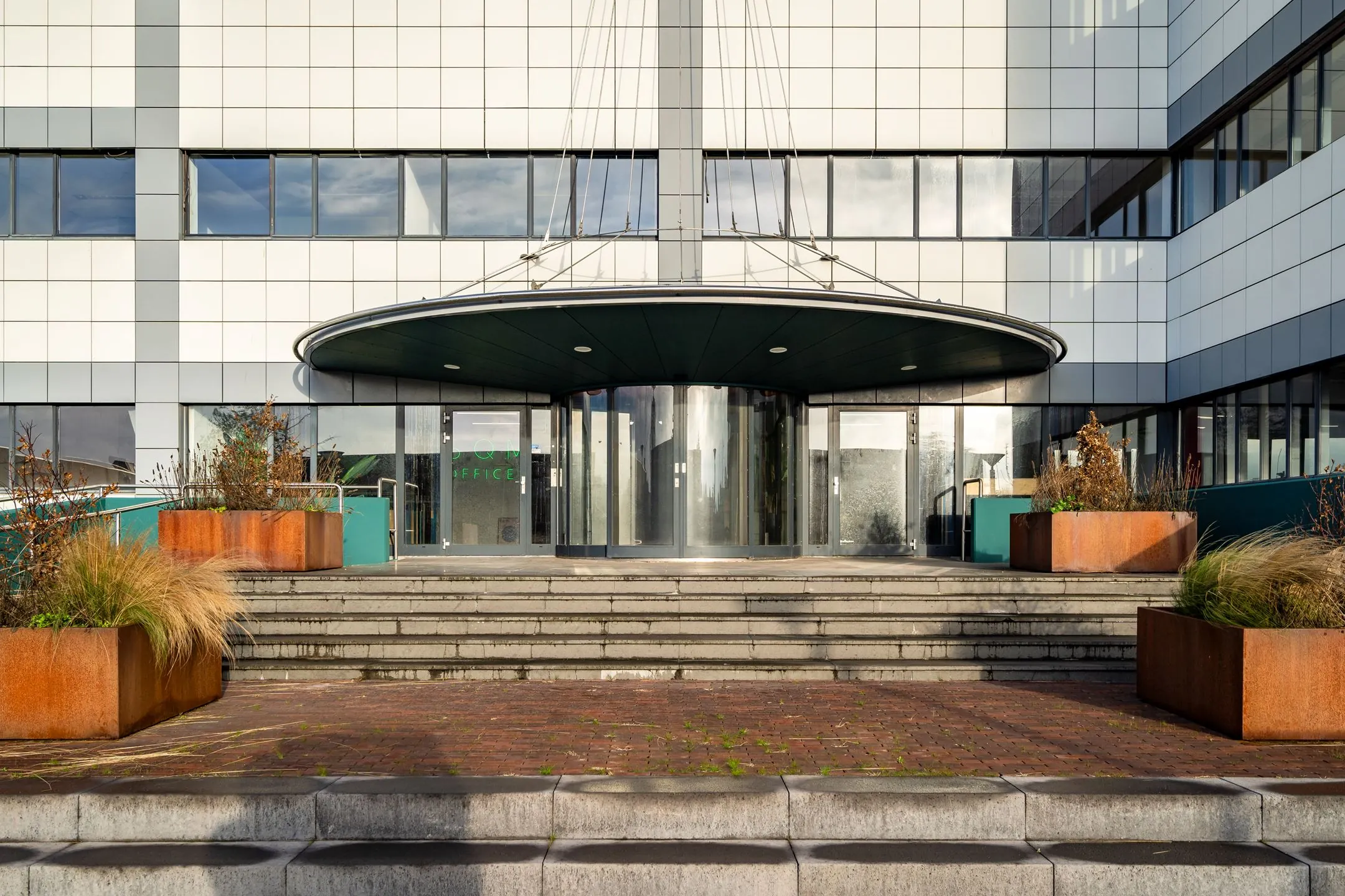 Vooraanzicht van de entree van een modern kantoorgebouw aan de Staverenstraat 15-17 in Deventer, met brede trappen en plantenbakken.