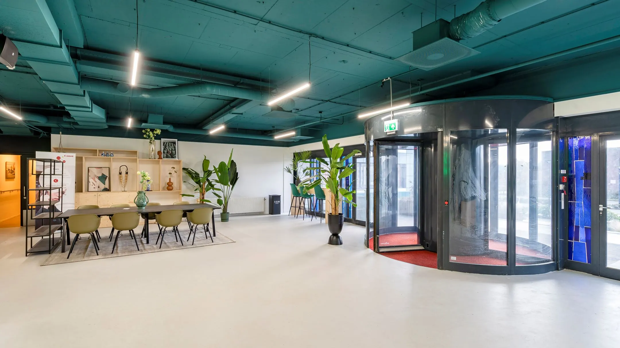 Moderne entree met een vergadertafel, planten en een glazen draaideur in kantoorruimte aan de Staverenstraat 15-17 in Deventer.