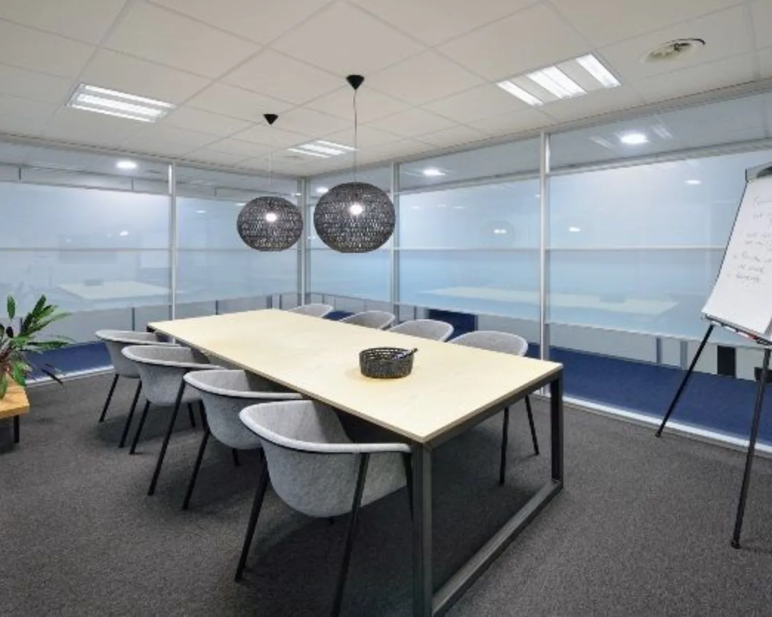 Moderne vergaderruimte met glazen wanden, een lange tafel, grijze stoelen en twee hanglampen in kantoor aan de Europalaan 2 in Den Bosch.