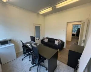 Moderne kantoorruimte met twee bureaus, een zwarte bank en een kleine kitchenette aan de Frans van Mierisstraat 50d in Amsterdam.