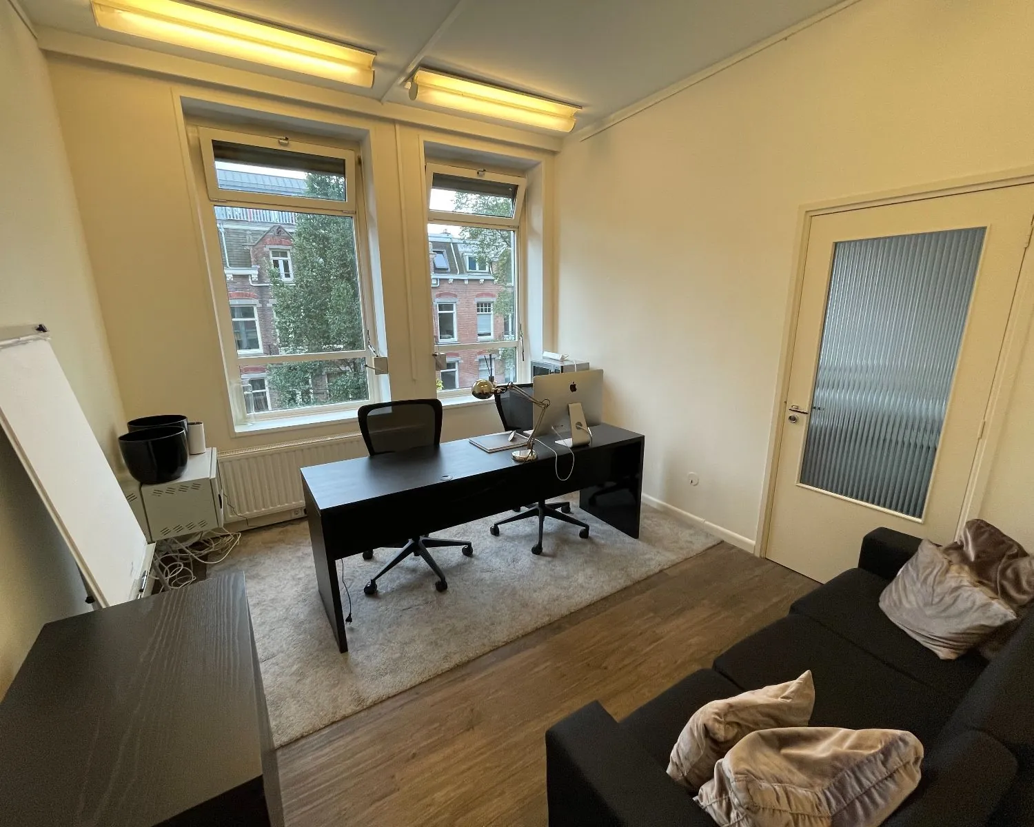 Moderne kantoorruimte met bureau, zithoek en grote ramen aan de Frans van Mierisstraat in Amsterdam.