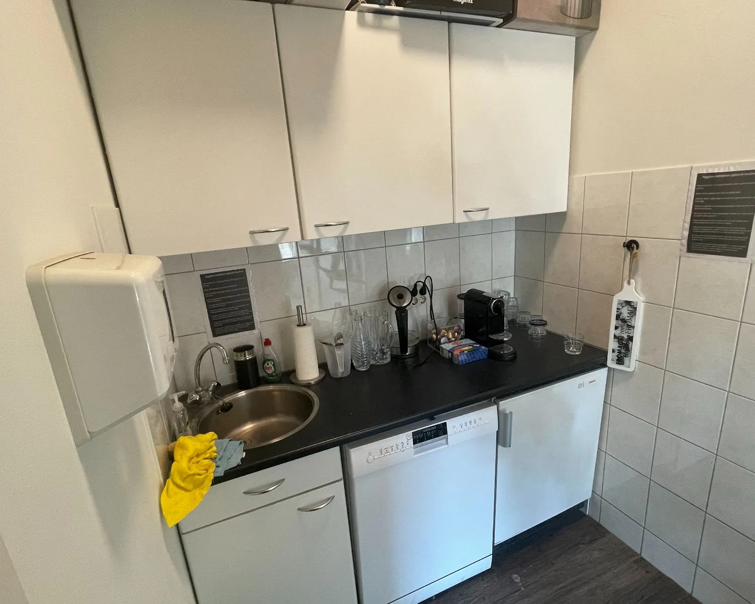 Kleine pantry met witte kasten, een vaatwasser, koffiezetapparaat en spoelbak in een kantoorruimte aan de Frans van Mierisstraat 50d in Amsterdam.