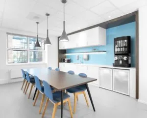 Moderne kantoorkeuken in Hilversum met lange vergadertafel, blauwe stoelen en koffieautomaat.
