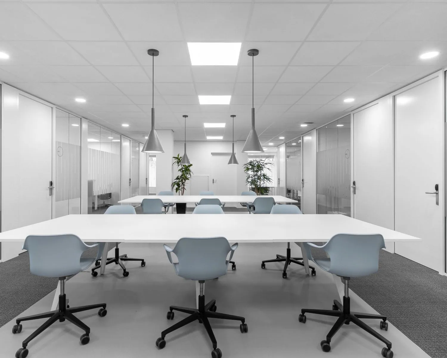 Moderne kantoorruimte in Hilversum met lange witte bureaus, lichtblauwe bureaustoelen en glazen scheidingswanden.