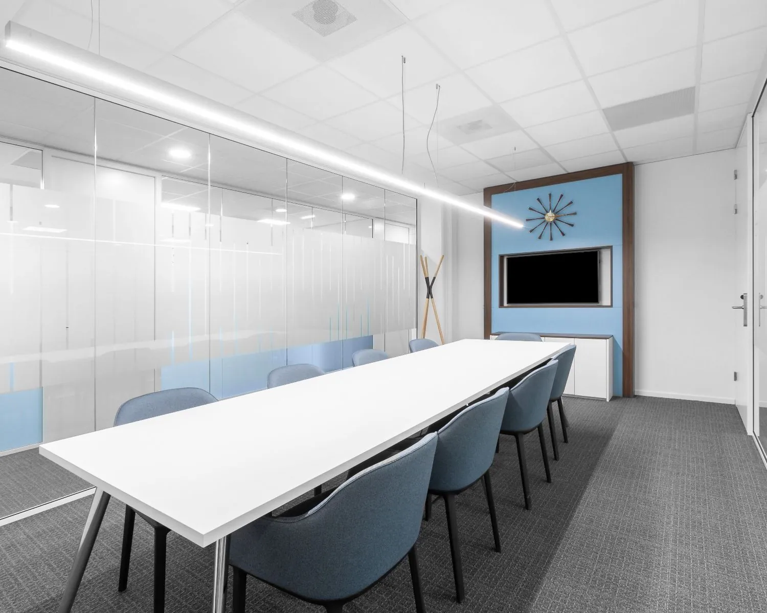 Moderne vergaderruimte in kantoor te huur aan Olympia 2d in Hilversum met glazen wand, lang witte tafel en blauwe stoelen.