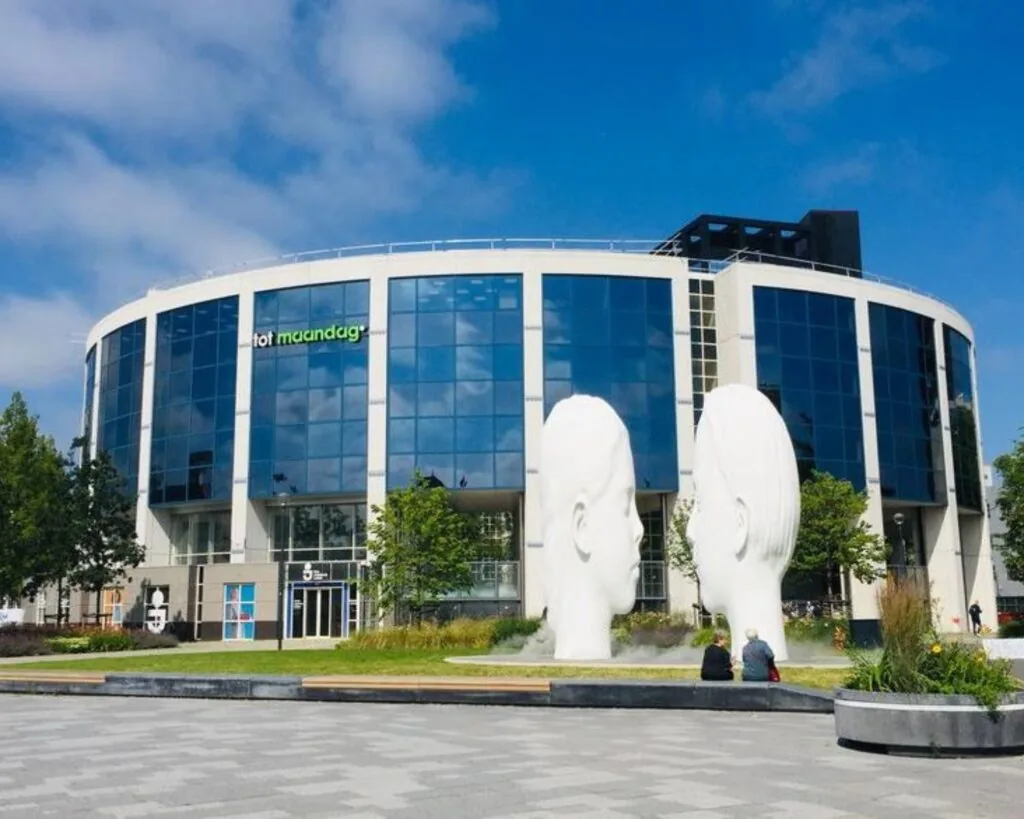Moderne kantoorruimte aan de Lange Marktstraat 1 in Leeuwarden met glazen gevel en twee grote witte sculpturen op het plein ervoor.