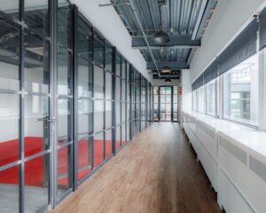 Moderne gang met glazen kantoorwanden en houten vloer in een kantoorgebouw aan de Oude Apeldoornseweg 41-45 in Apeldoorn.