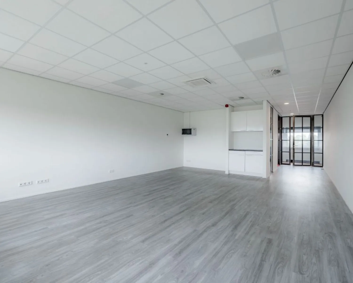 Lichte en moderne kantoorruimte met grijze vloer, systeemplafond en glazen deuren aan de Oude Apeldoornseweg in Apeldoorn.