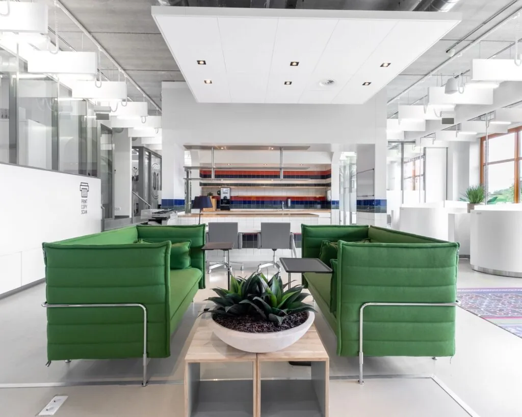 Moderne kantoorruimte op het Piet Mondriaanplein met groene zitbanken, een grote plant en een open keuken in kleurrijke tegels.