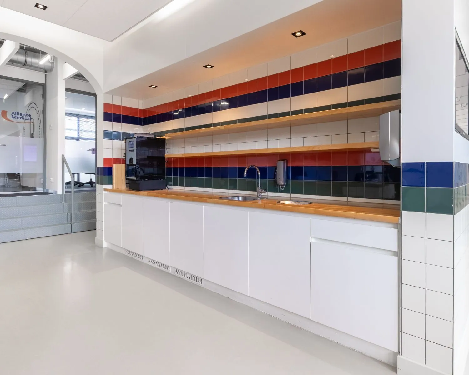 Moderne pantry in een kantoorruimte aan het Piet Mondriaanplein met gekleurde tegelwand en witte kasten.