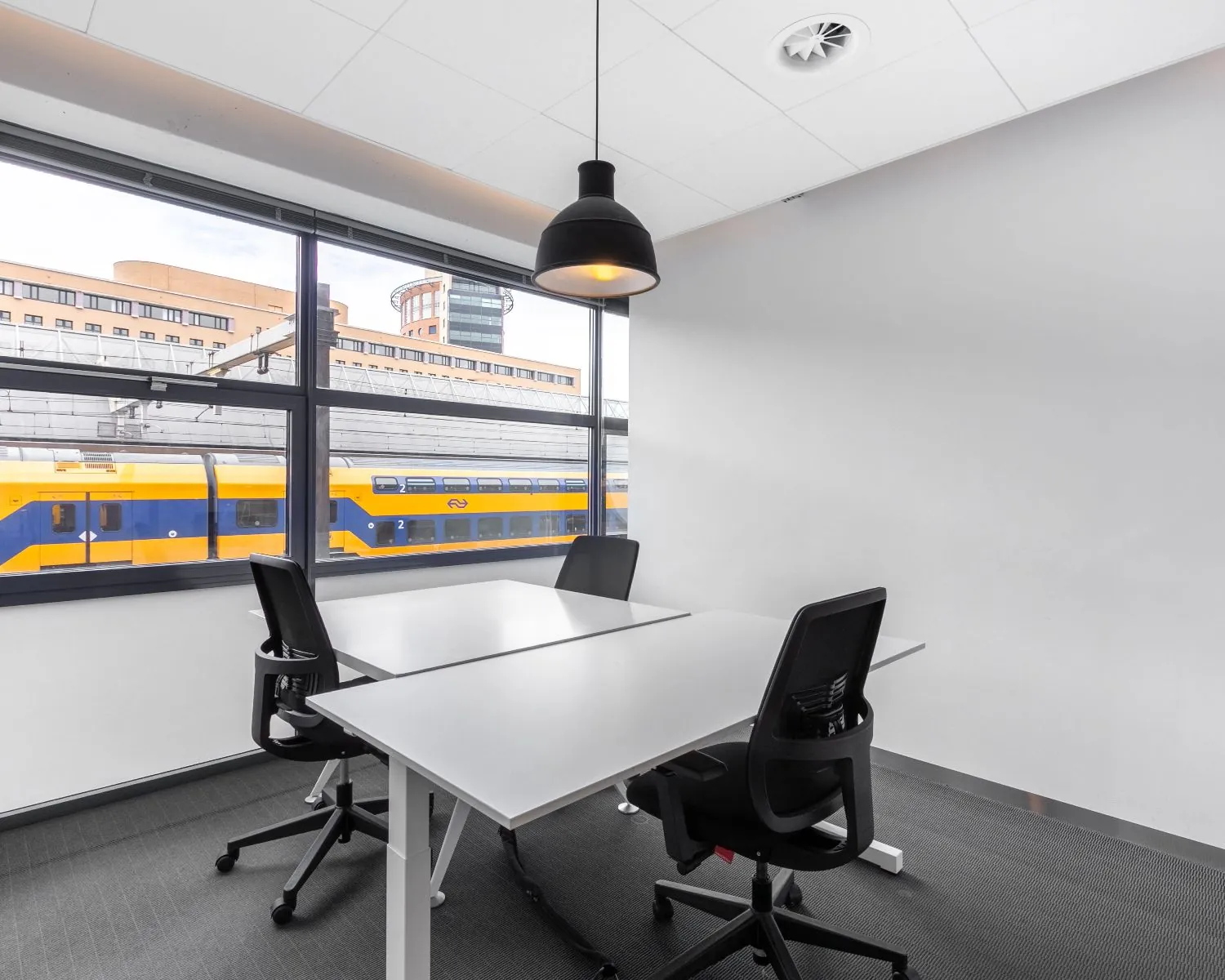 Moderne kantoorruimte met twee bureaus en uitzicht op een passerende NS-trein bij Piet Mondriaanplein 13.