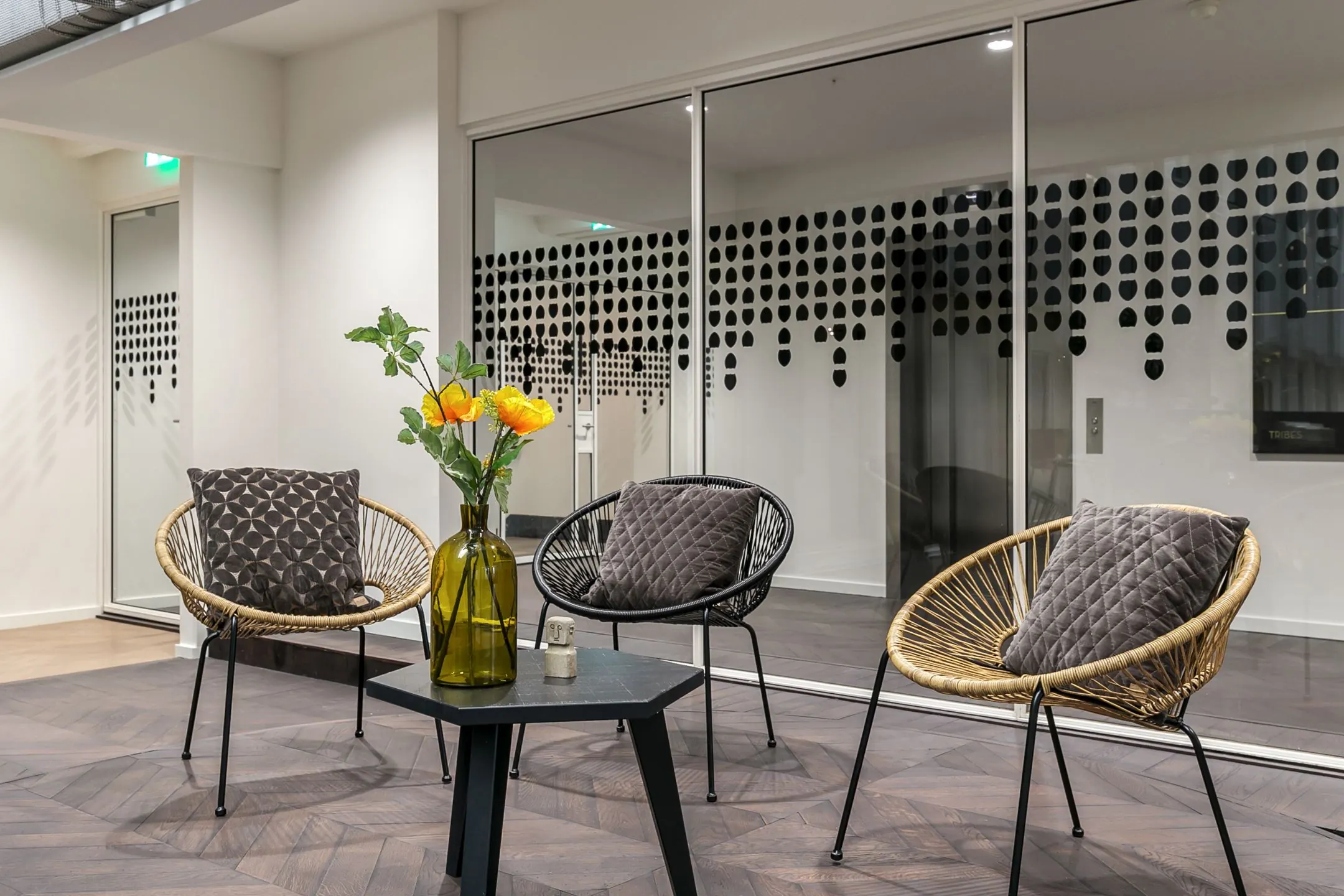 Moderne wachtruimte bij kantoorruimte te huur aan Rotterdam Blaak 34, met stijlvolle stoelen, sierkussens en een glazen wand met decoratief patroon.