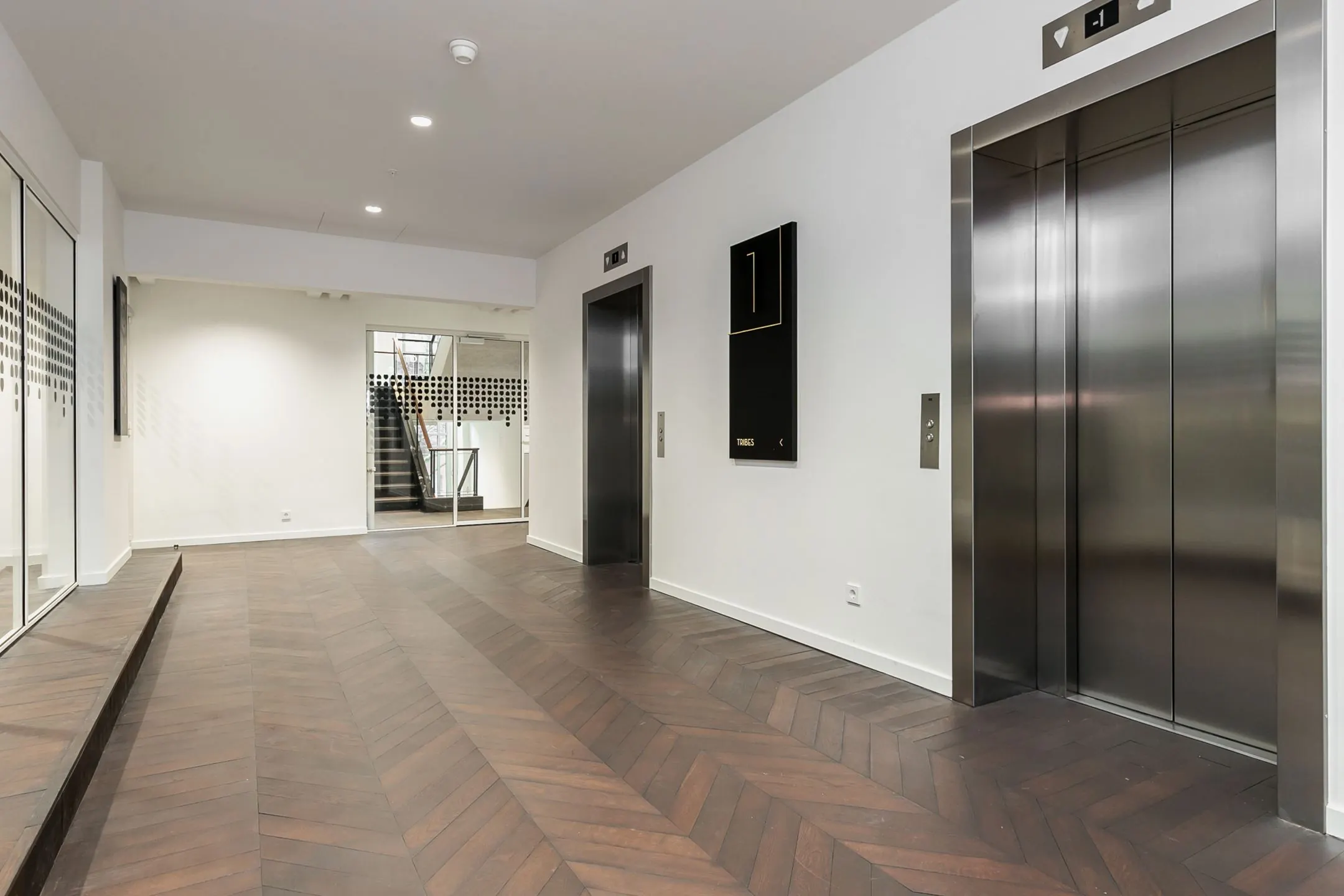 Moderne kantoorhal met houten visgraatvloer, liften en glazen deur bij Blaak 34 in Rotterdam.