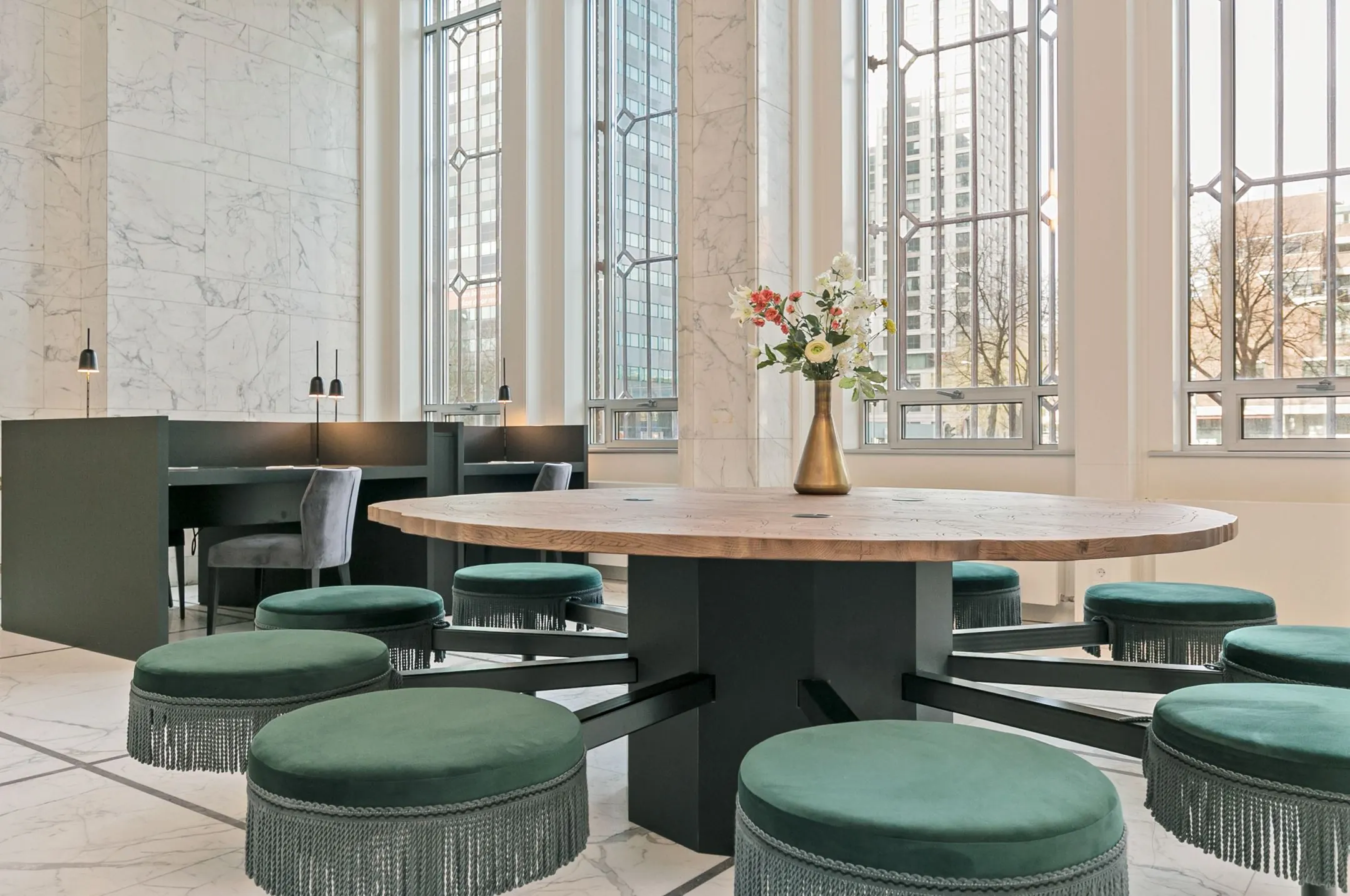 Moderne kantoorruimte aan Rotterdam Blaak 34 met een ronde houten tafel, groene krukjes en hoge ramen met uitzicht op de stad.