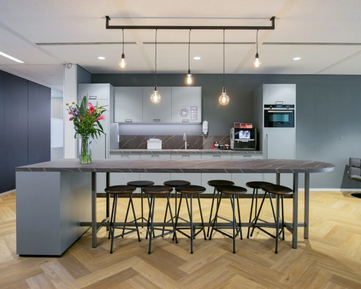 Moderne kantoorkeuken met hoge tafel, barkrukken en ingebouwde apparatuur in een ruimte aan het Alexanderveld in Den Haag.