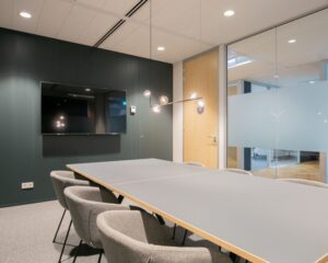 Moderne vergaderruimte in kantoor aan het Alexanderveld 5 in Den Haag met glazen wanden, grijze stoelen en een flatscreen aan de muur.