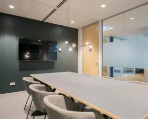 Moderne vergaderruimte in kantoor aan het Alexanderveld 5 in Den Haag met glazen wanden, grijze stoelen en een flatscreen aan de muur.