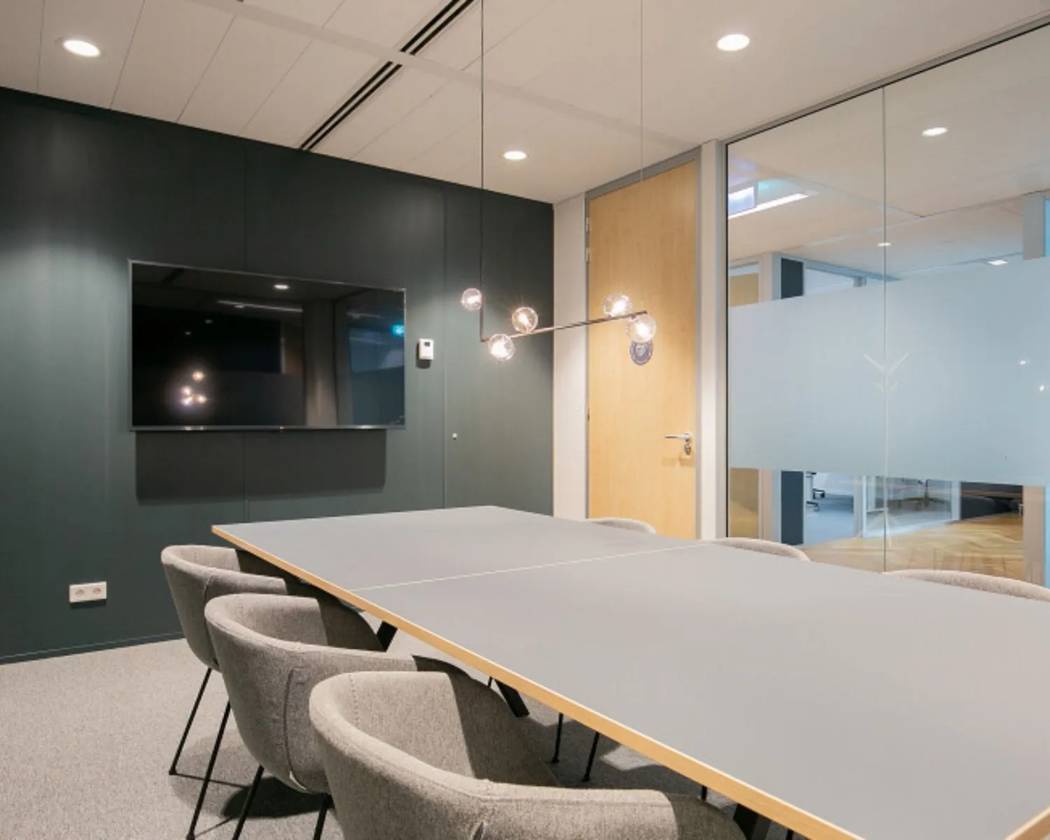 Moderne vergaderruimte in kantoor aan het Alexanderveld 5 in Den Haag met glazen wanden, grijze stoelen en een flatscreen aan de muur.